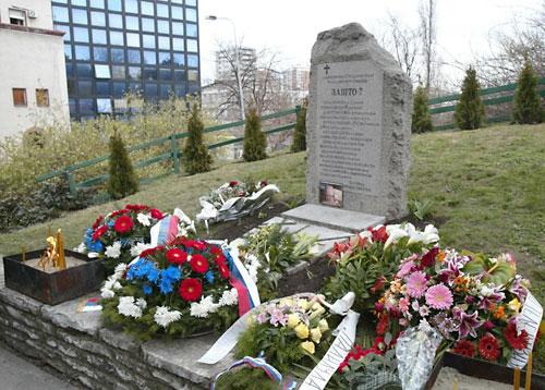 Flowers for the bombing's 16 victims are laid in front of a monument the 16 mourning families erected in Tasmajdan Park. The current RTS building can be seen in the background. Photo via B92.