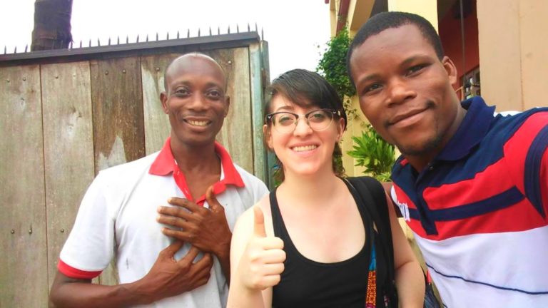 Libby Pollak giving a thumbs up with two Ghanaian men