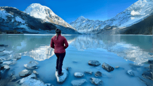 Person standing on the shores of a lake in between mountain peaks